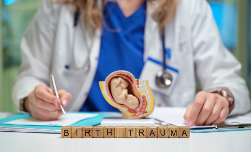 Doctor writing notes beside a fetal development model with wooden blocks spelling "birth trauma"