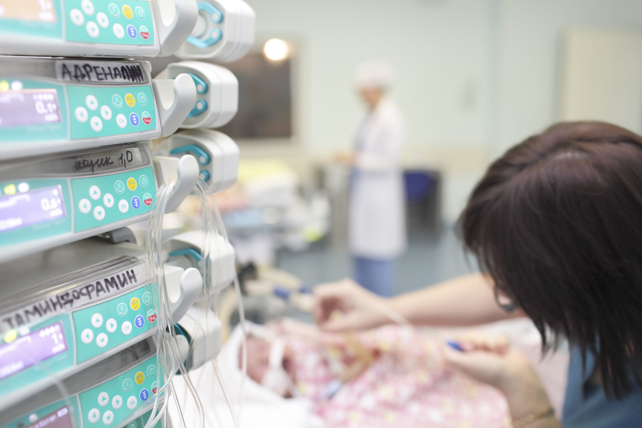 A mother reaches toward her newborn in a hospital incubator surrounded by medical monitoring equipment.